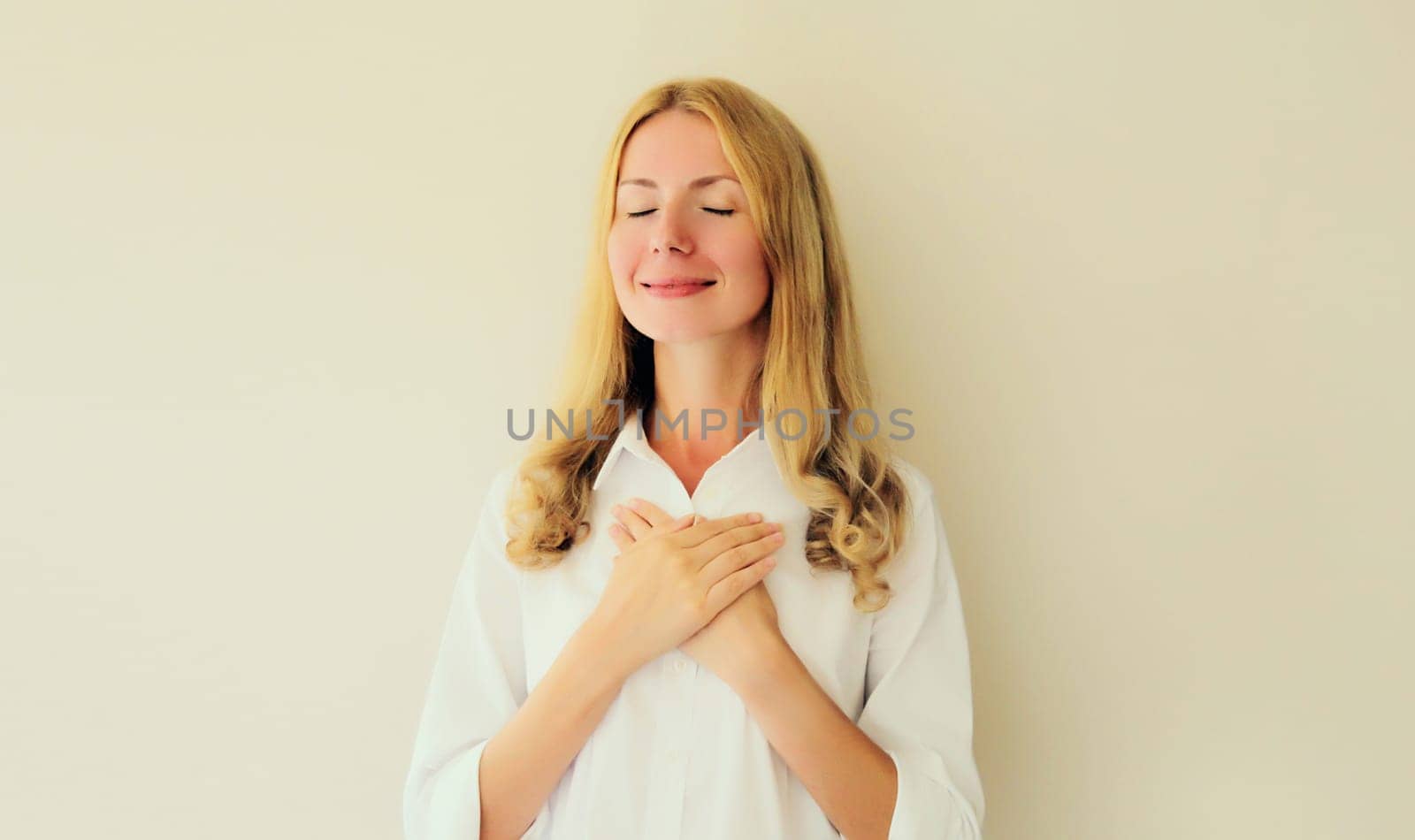 Portrait of beautiful happy smiling caucasian grateful woman put folded hands on her heart by Rohappy