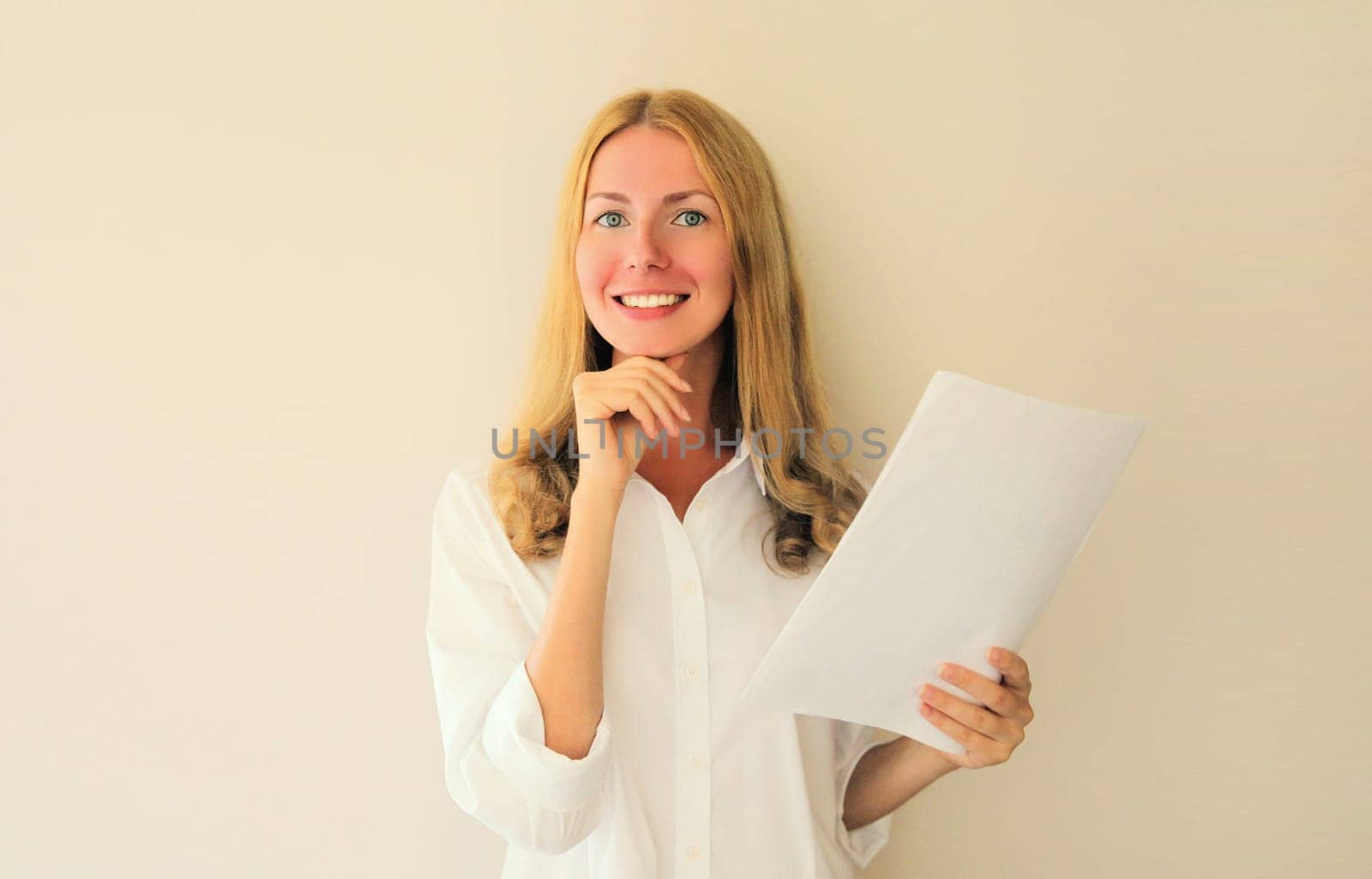 Portrait of happy smiling caucasian young woman employee with white blank sheet of paper document looking at camera in office