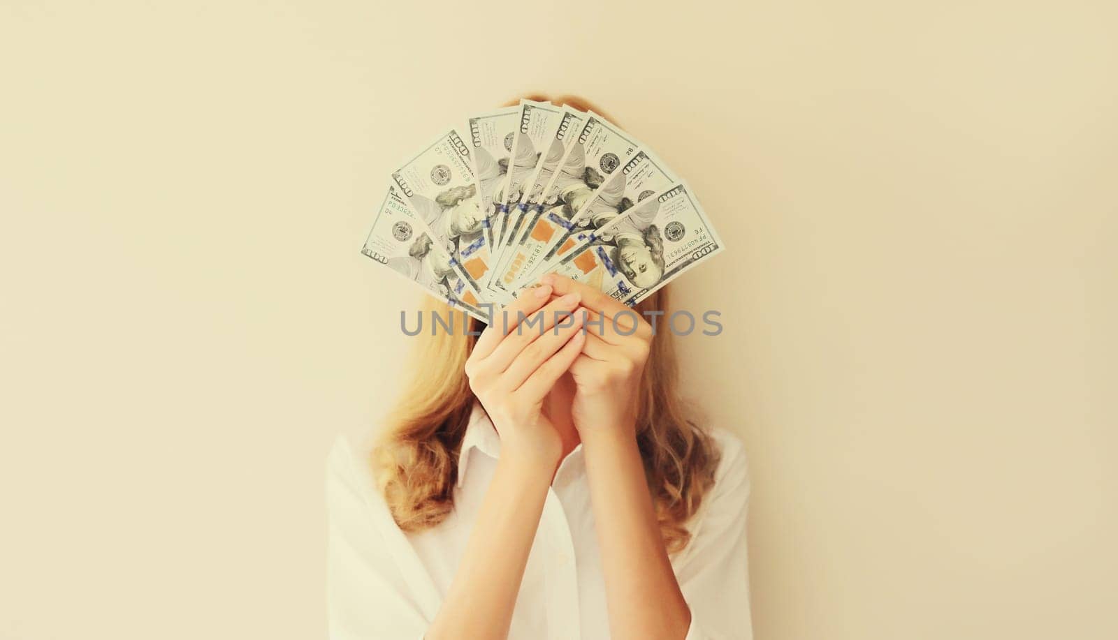Portrait of happy woman holding cash money in dollar bills in her hands covering her face