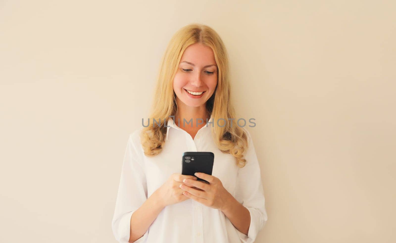 Portrait of happy smiling caucasian young woman 20s with mobile phone looking at device on studio background