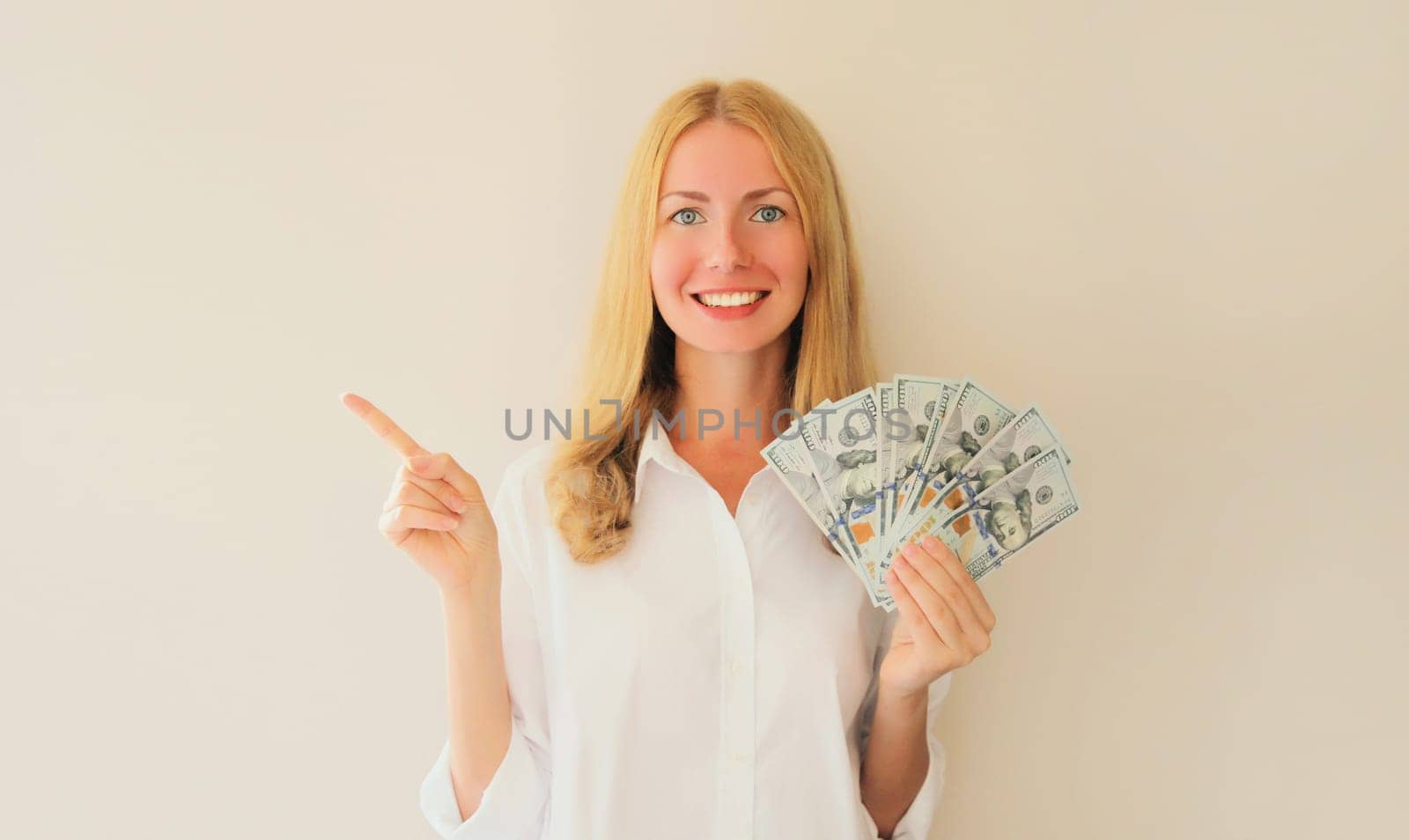 happy smiling young woman holding cash money in dollar bills in her hands and points her finger to the side, blank copy space for advertising text