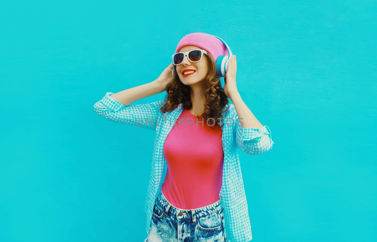 Portrait of stylish modern happy young woman listening to music with headphones in colorful clothes by Rohappy