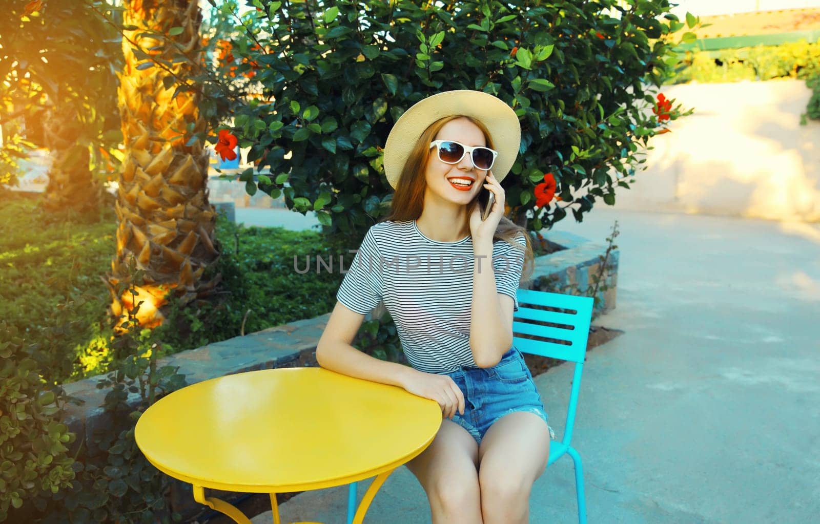 Happy young woman calling on mobile phone sitting on the table in street cafe by Rohappy