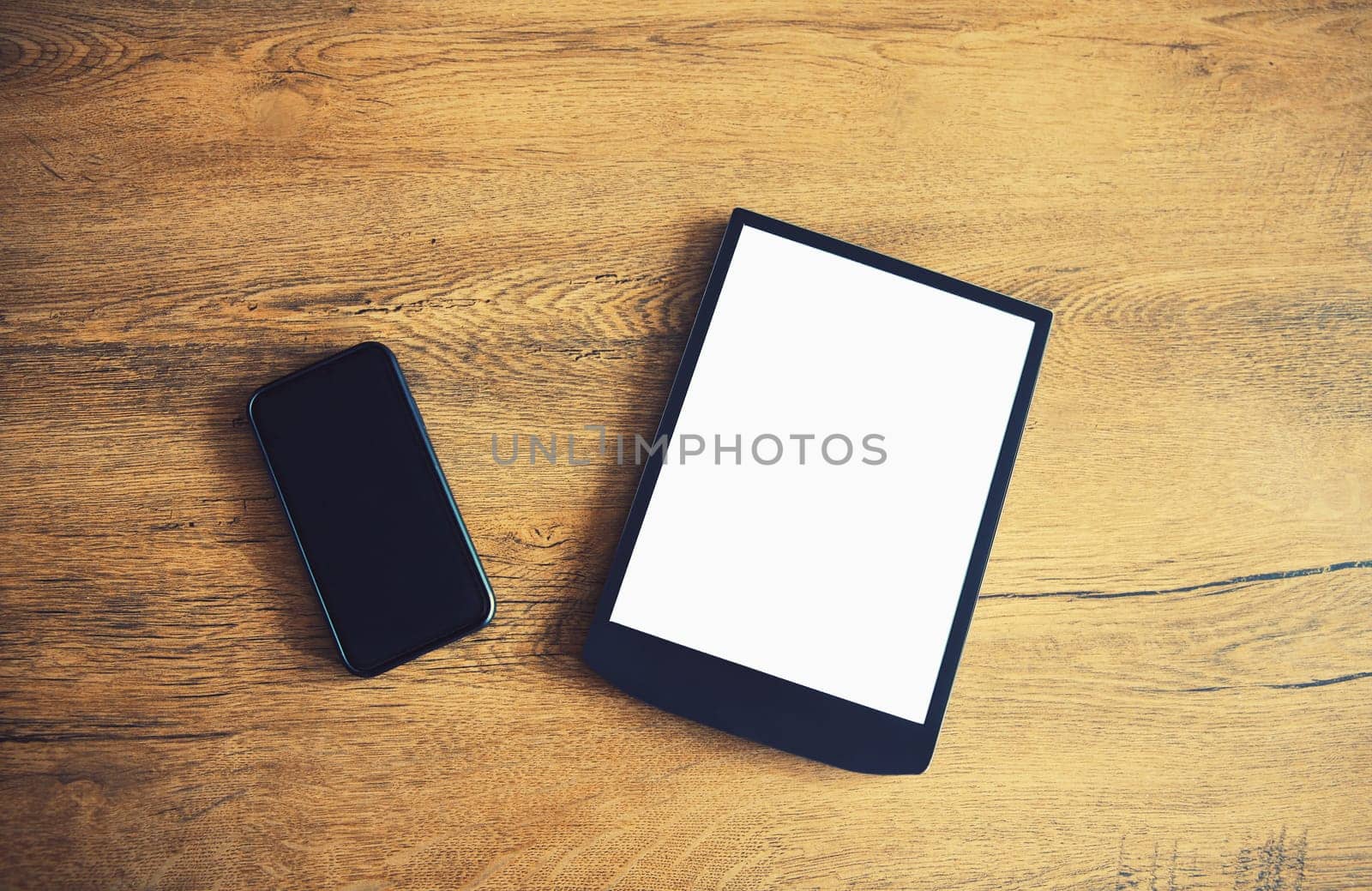 White blank screen digital tablet computer and black mobile phone on wooden table at home, top view