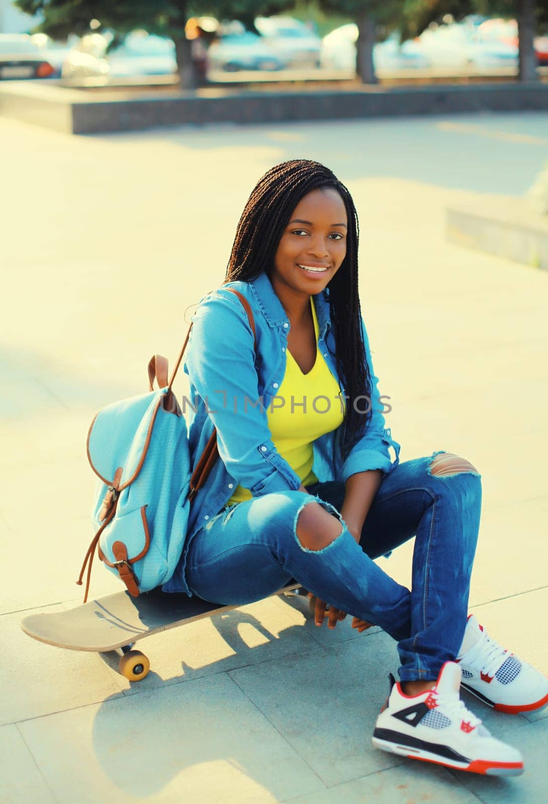 Portrait of happy smiling young african woman model posing with skateboard in the city