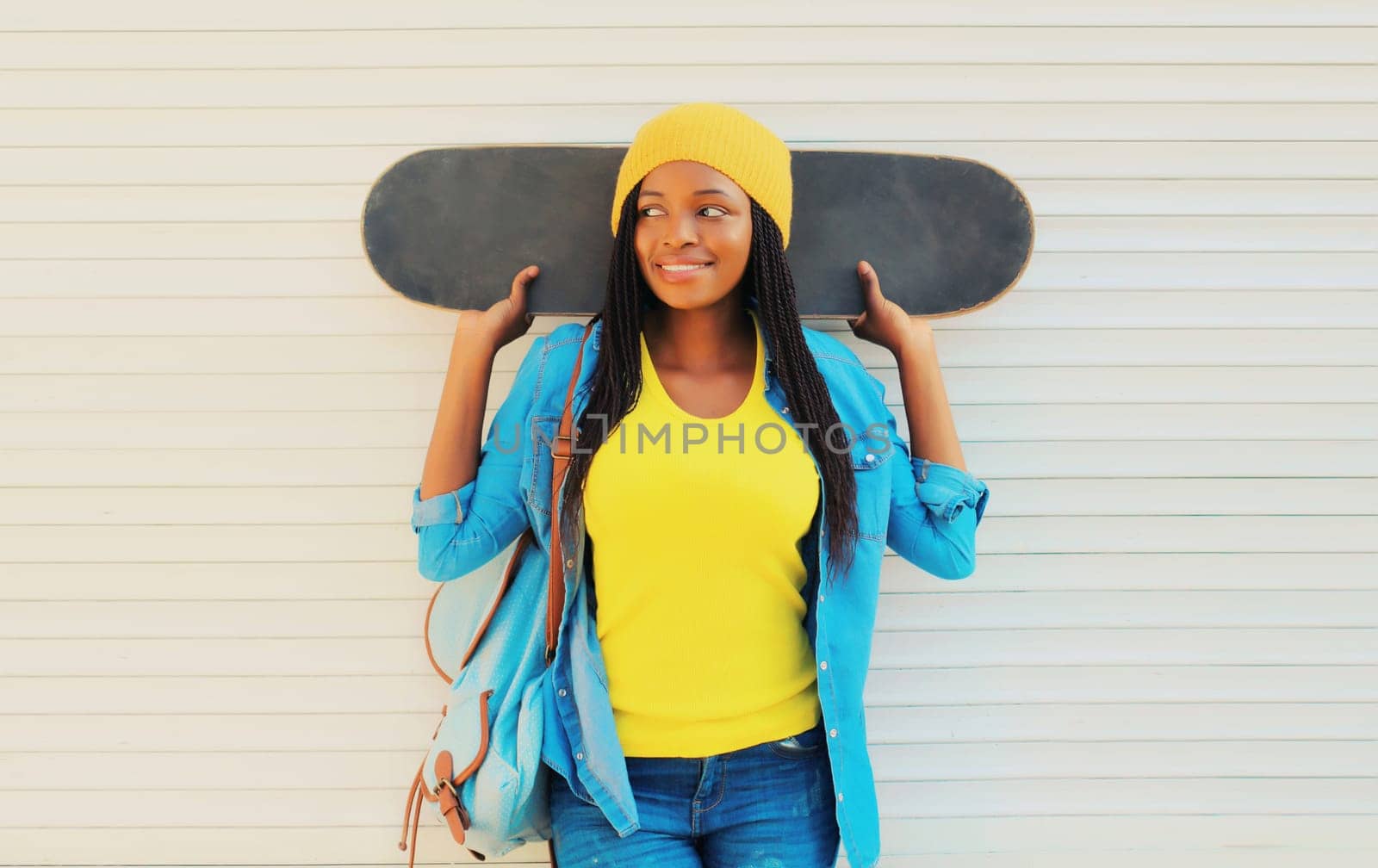 Portrait of happy smiling young african woman model posing with skateboard in the city