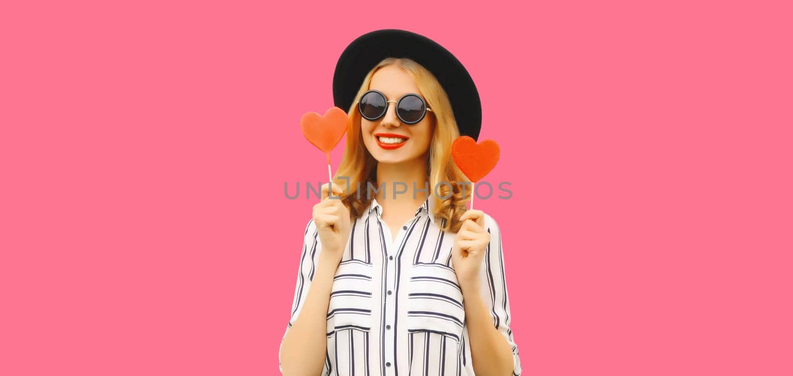 Portrait of happy cheerful young woman with sweet red heart shaped lollipop on stick on pink by Rohappy