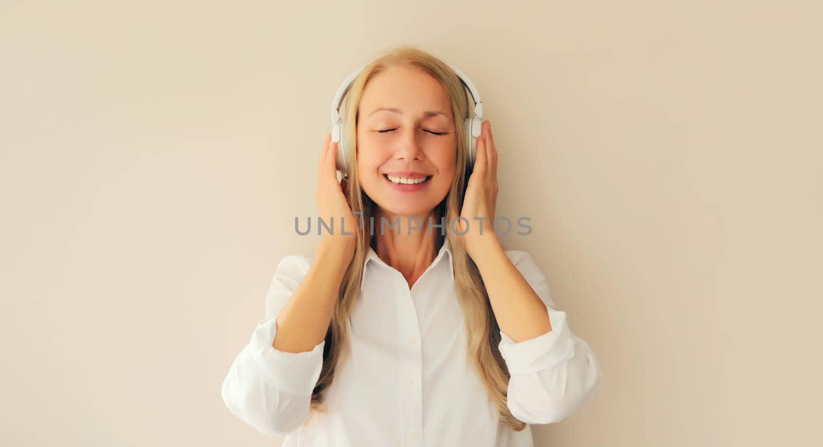 Portrait of happy relaxed middle aged woman listening to music in wireless headphones on white background