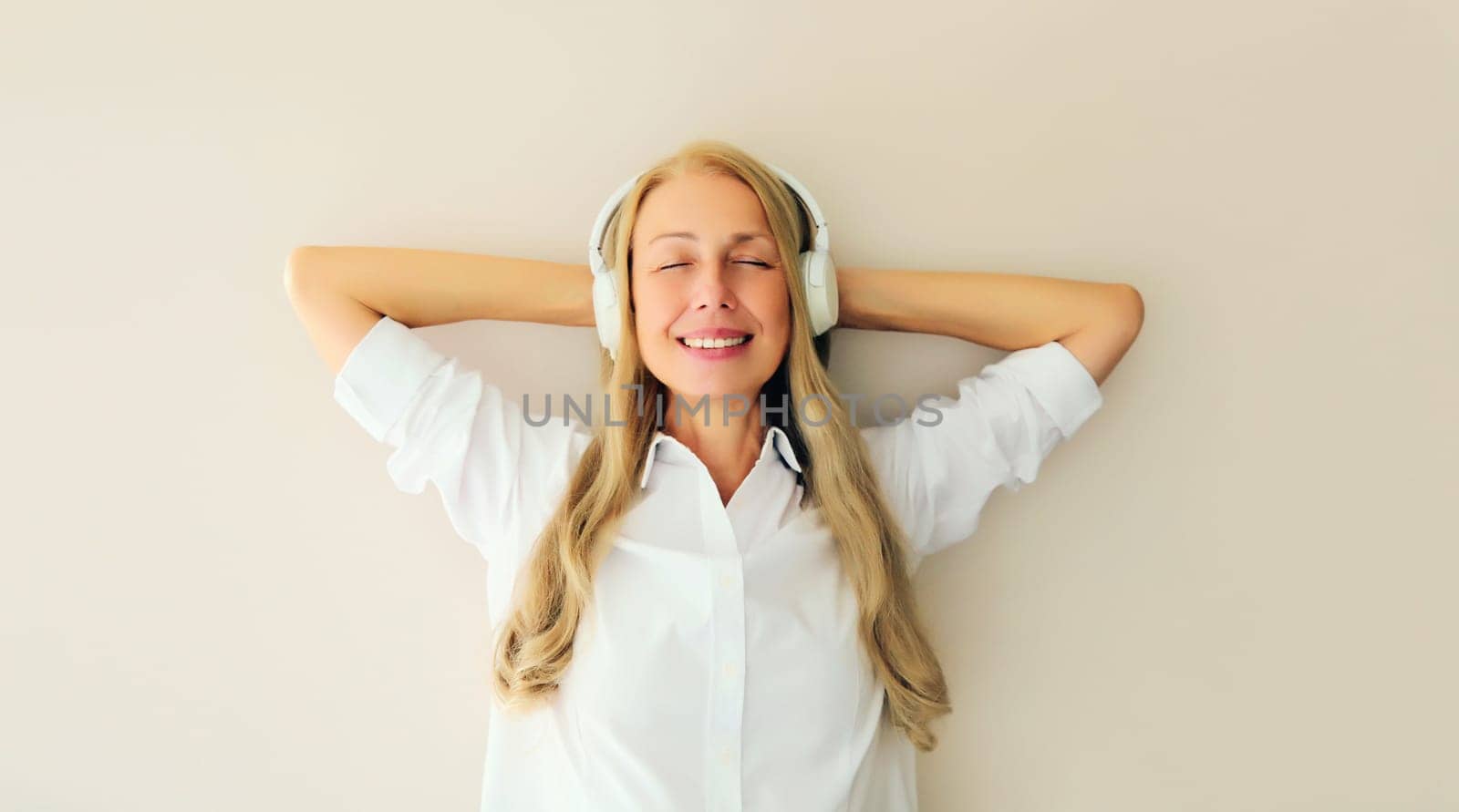 Portrait of happy relaxed middle aged woman listening to music in wireless headphones on white background