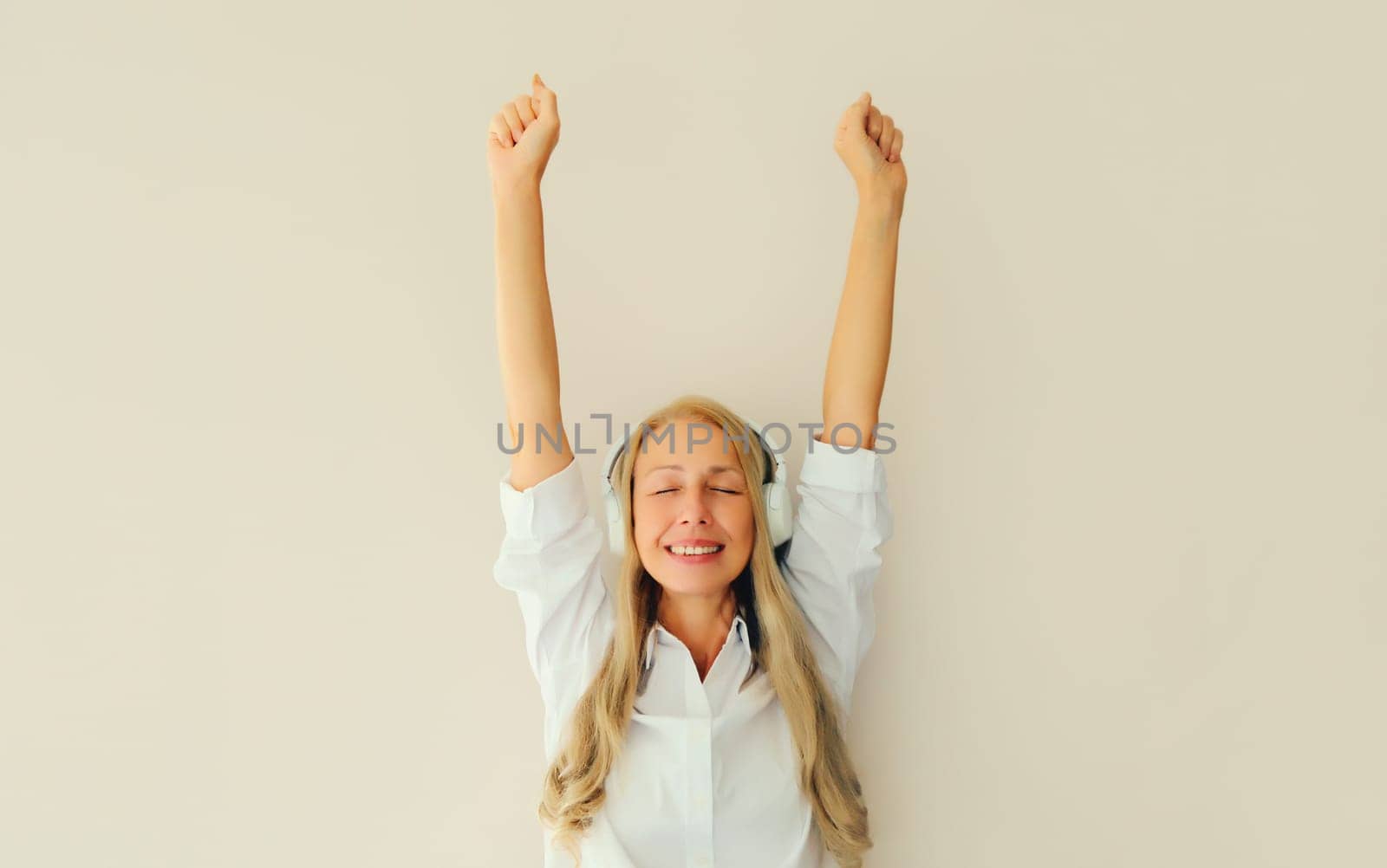 Happy cheerful middle aged woman listening to music dancing having fun in headphones on white background