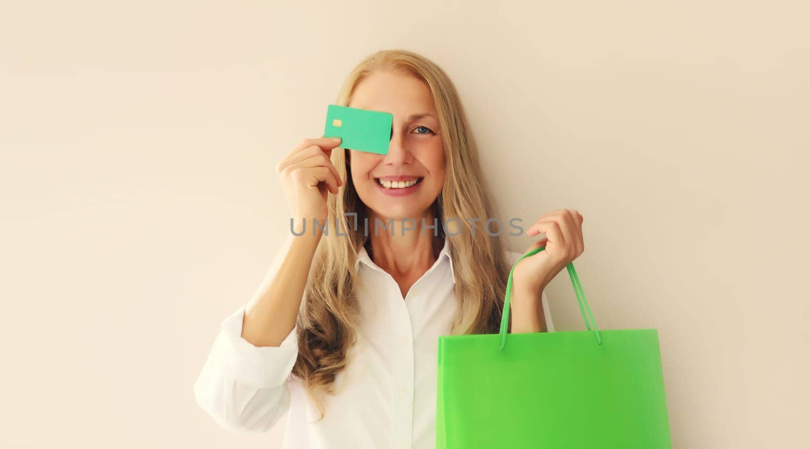 Portrait of happy smiling caucasian middle aged woman holding plastic credit bank card with shopping bags on studio background