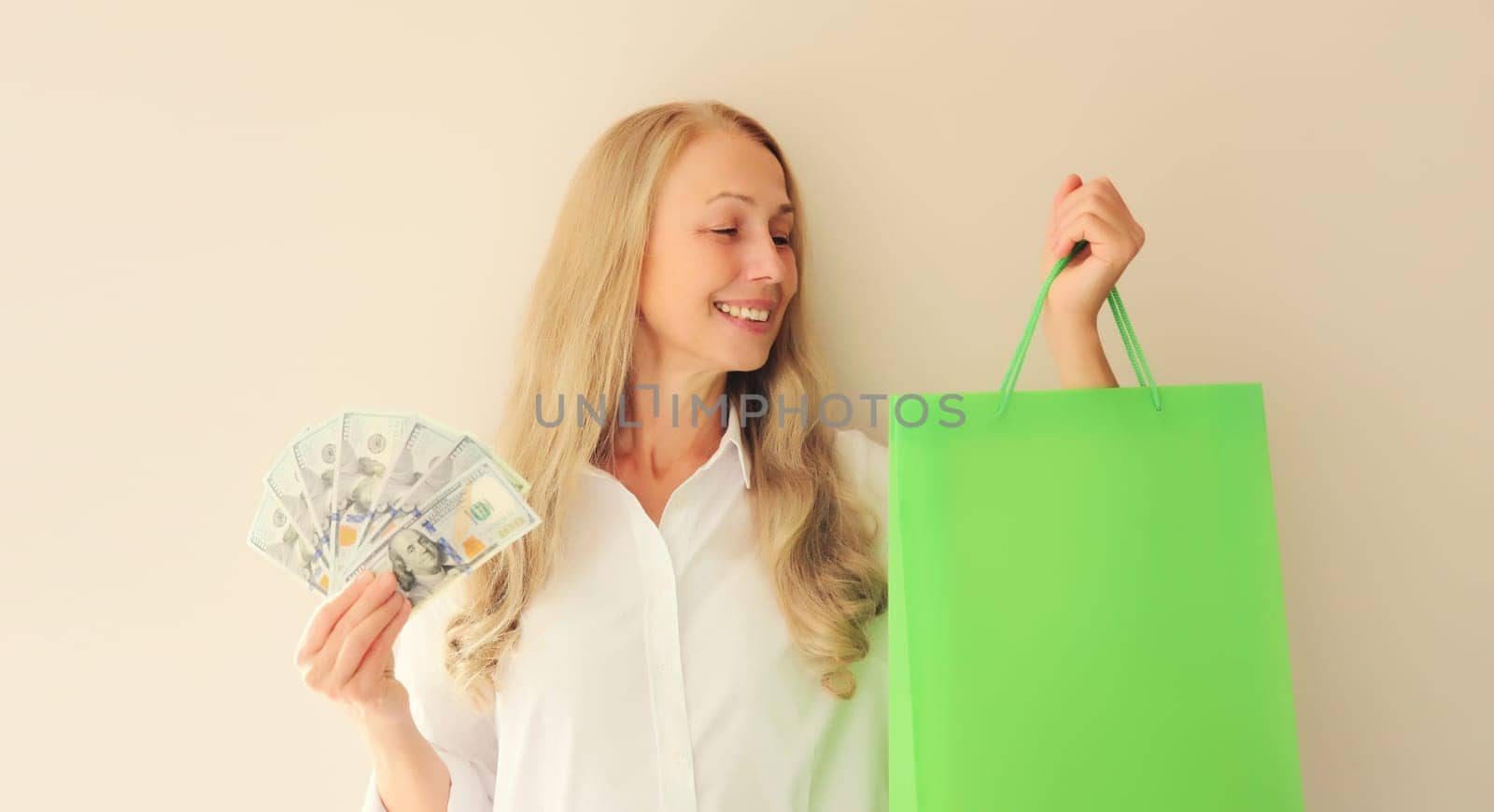 Portrait of happy smiling middle aged woman with shopping bags holding cash money in dollar bills in her hands