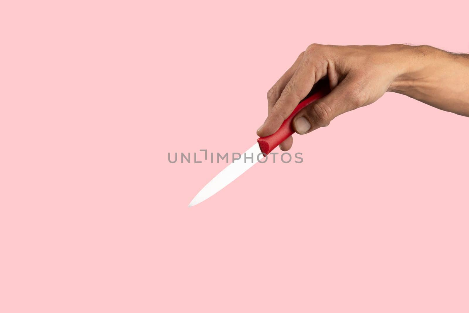 Black male hand holding a red cooking knife isolated pink background. High quality photo