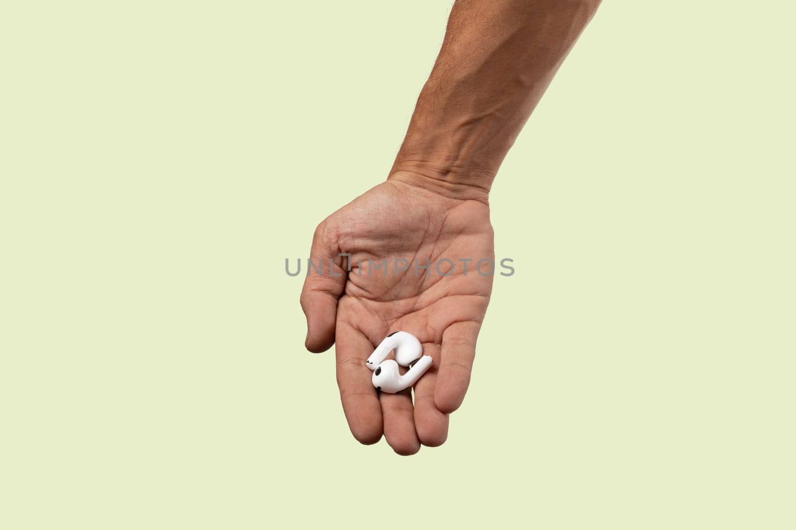 Male hand holding white earbuds on light green background. High quality photo