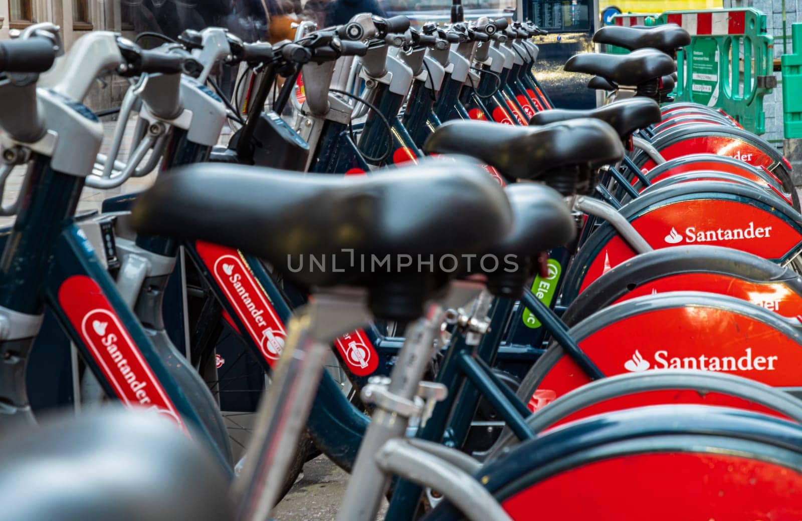 London, UK - Feb 15, 2024 - Public rental bicycle for transportation bike to work and travel in center city of London, View of Bicycle seat and Bicycle handlebars, Row of Urban electric red bikes charging batteries, Urban transport, Shared rental bike, Space for text, Selective focus.