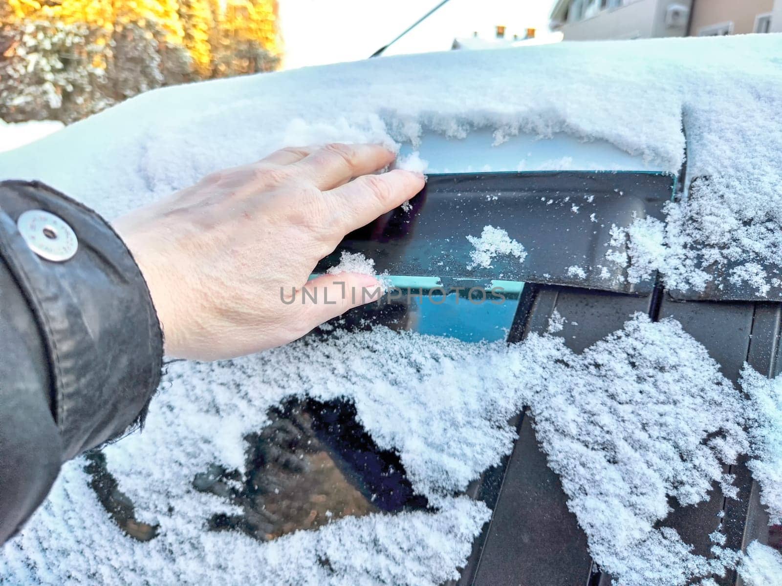 Hand of Woman persons brushing snow of car window, which frozen over during a bitterly cold morning. Problem with travel and trip in winter
