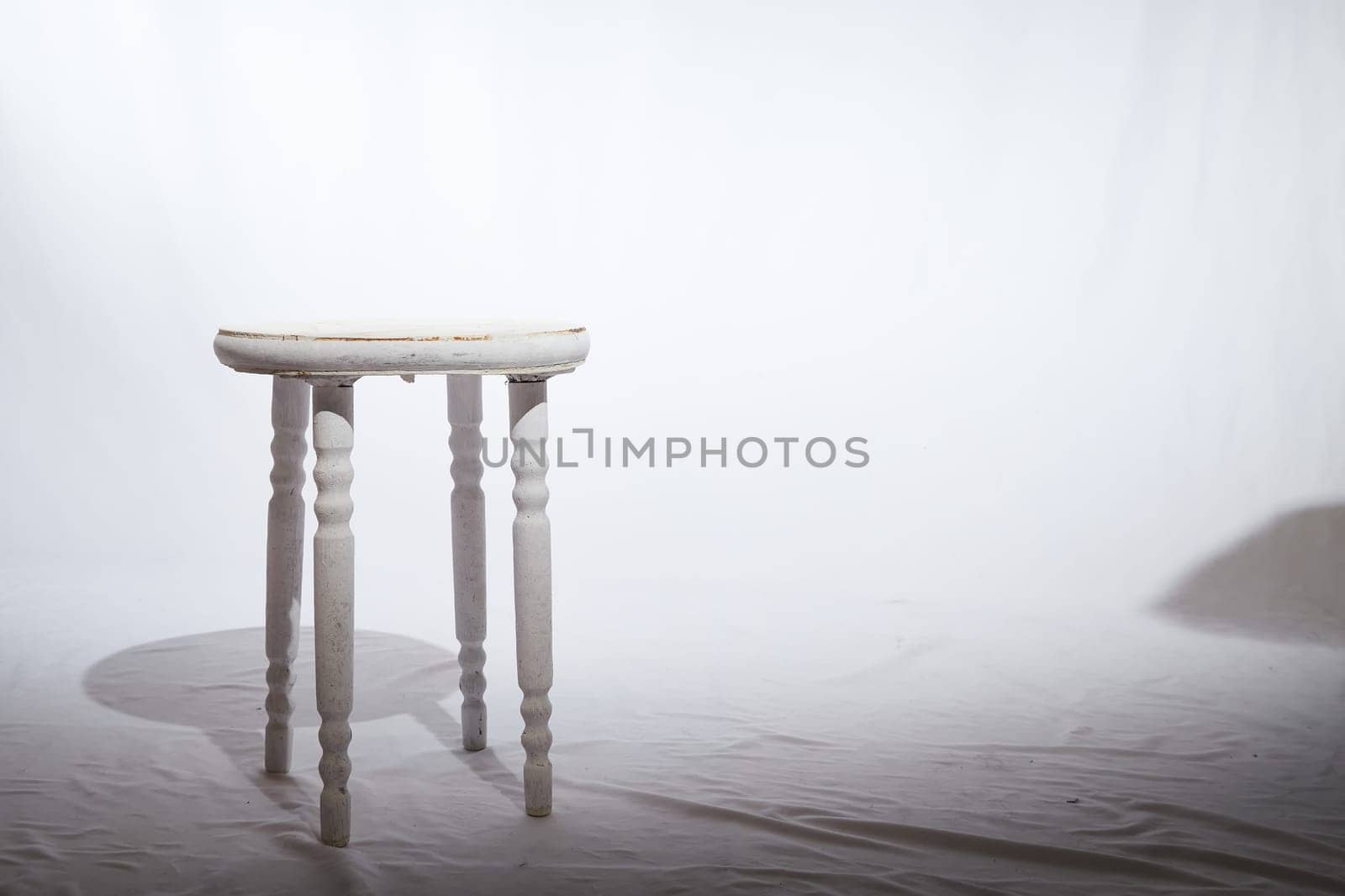 Solitary Wooden Stool in a White Minimalist Setting. Lone, white-painted wooden stool stands centered on textured surface, surrounded by soft white backdrop