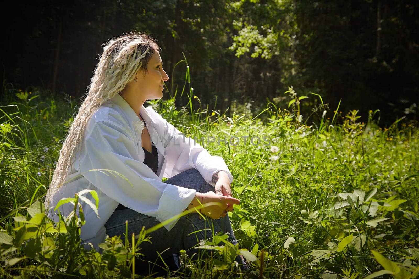 Kirov, Russia - June 12, 2023: Hippy girl enjoys life in forest on a sunny spring or summer day. Woman in green nature landscape