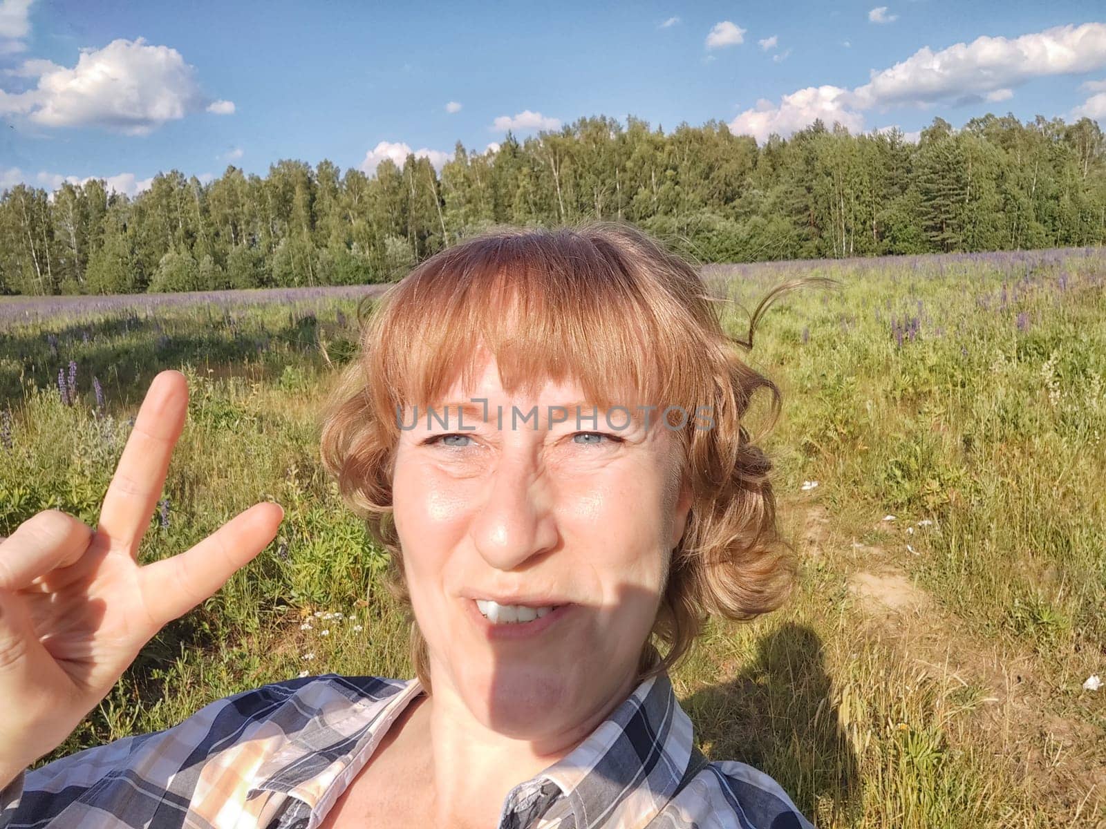 Happy female blonde tourist taking selfie picture with smart mobile phone outside. Middle aged woman having fun on adventure trip on nature by keleny