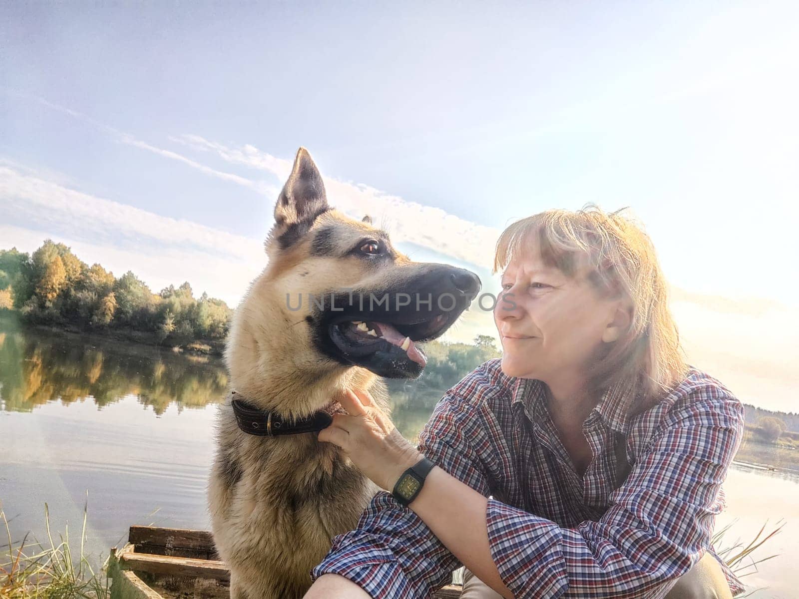 Adult girl with shepherd dog taking selfie in forest. Middle aged woman and big shepherd dog on nature. Friendship, love, fun, hugs