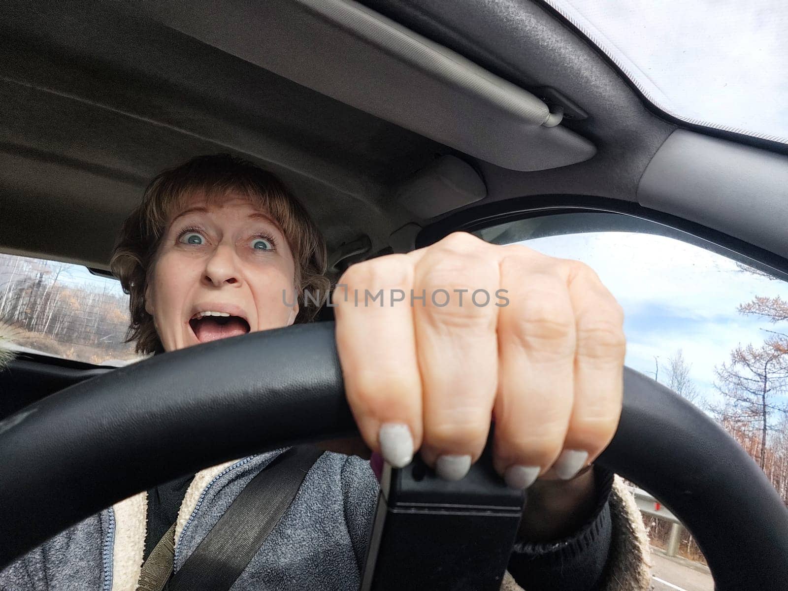 Terrified female driver a second before the accident. Scared middle-aged adult woman holds the steering wheel of car. Frightened Lady girl who is owner or rent a car for travel