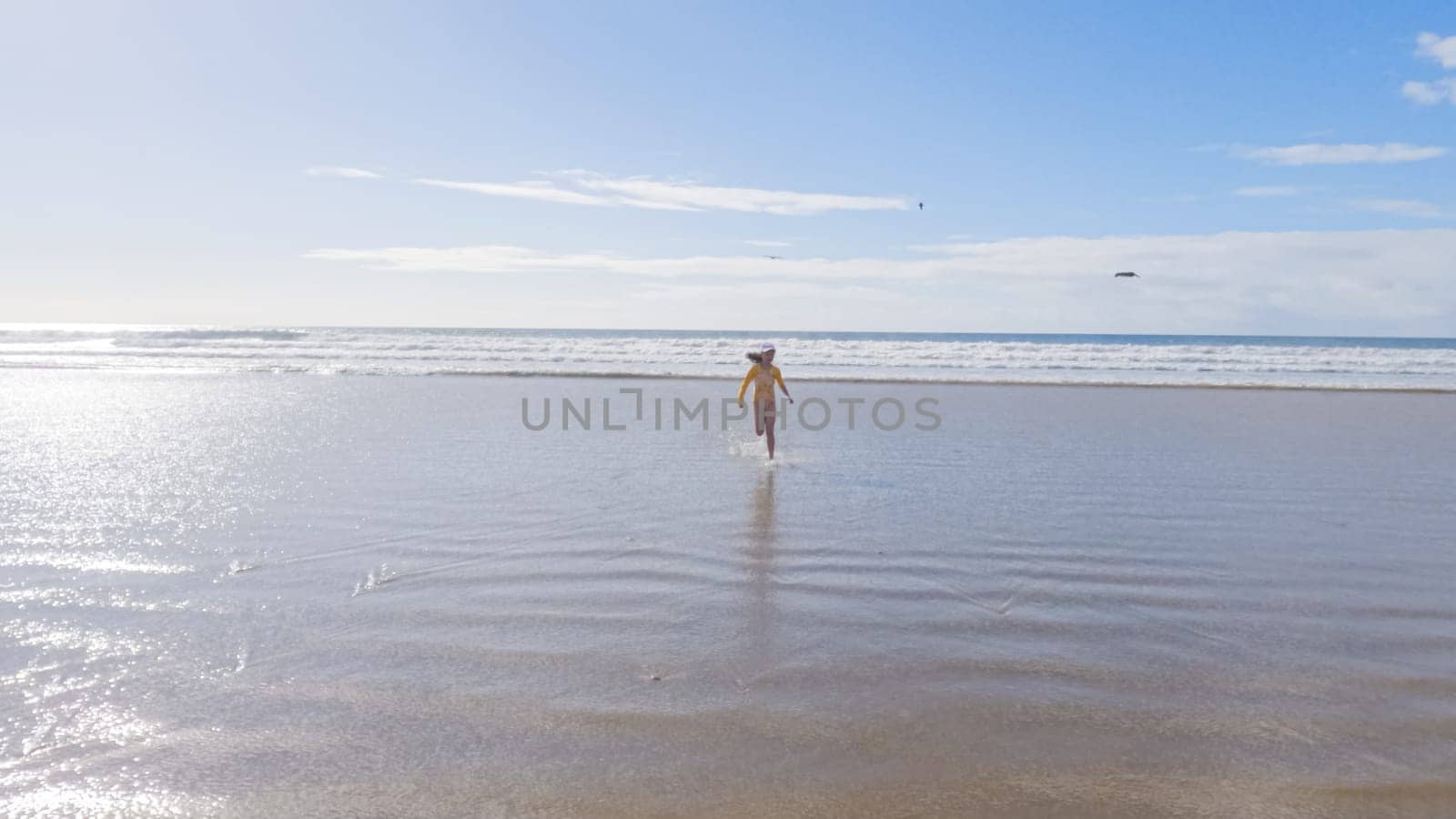 Little girl, braving the cold, joyfully runs in her swimsuit across the beach during winter.