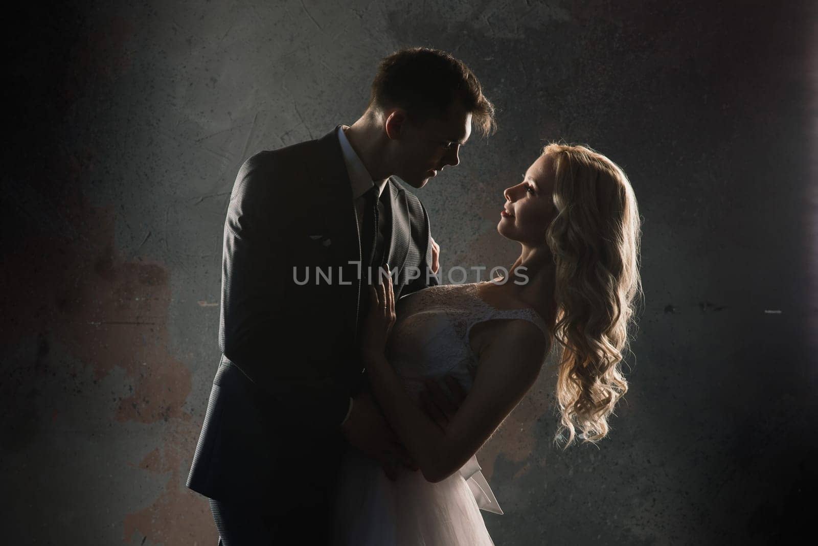 Cute wedding couple in the interior of a classic studio. They kiss and hug each other.