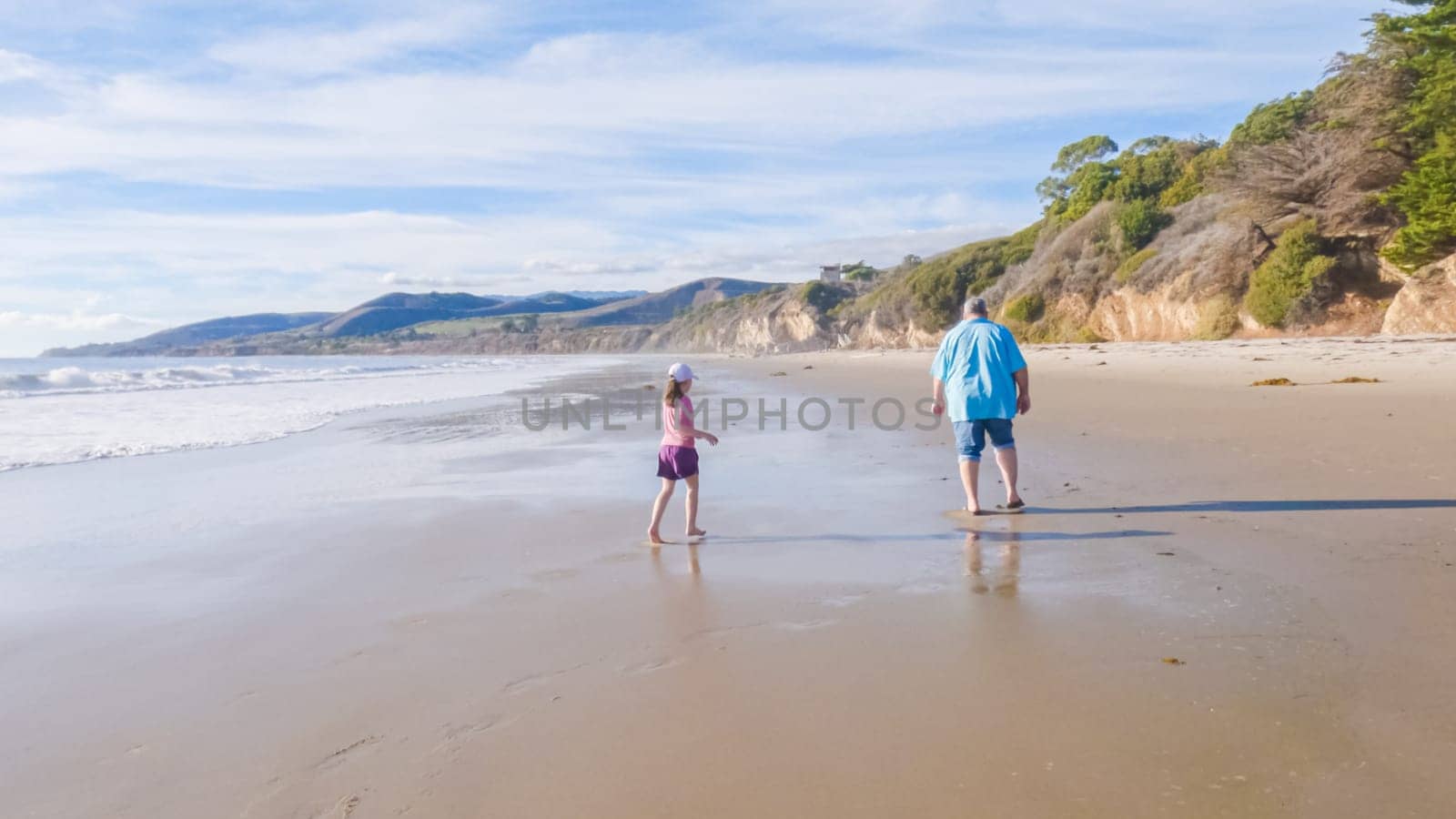 In California, a father and daughter share a serene winter walk along the deserted sands of El Capitan State Beach.