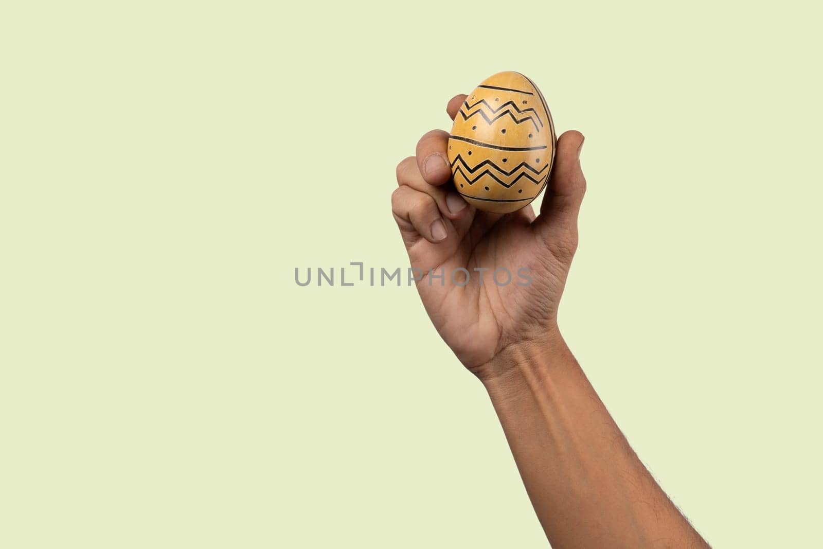 Male hand holding modern painted easter egg on light green background. High quality photo