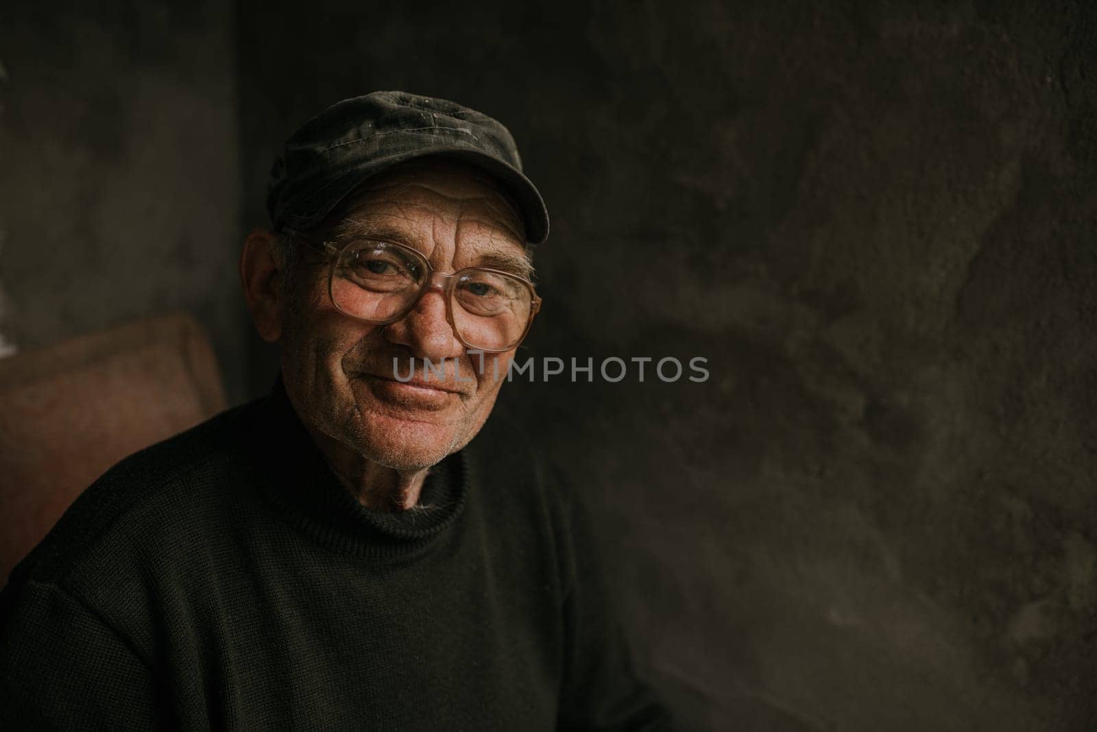 Pensive old man in glasses with gray hair looks away. wrinkles. wisdom. against a dark gray texture wall. bald head. in a knitted sweater. Portrait.