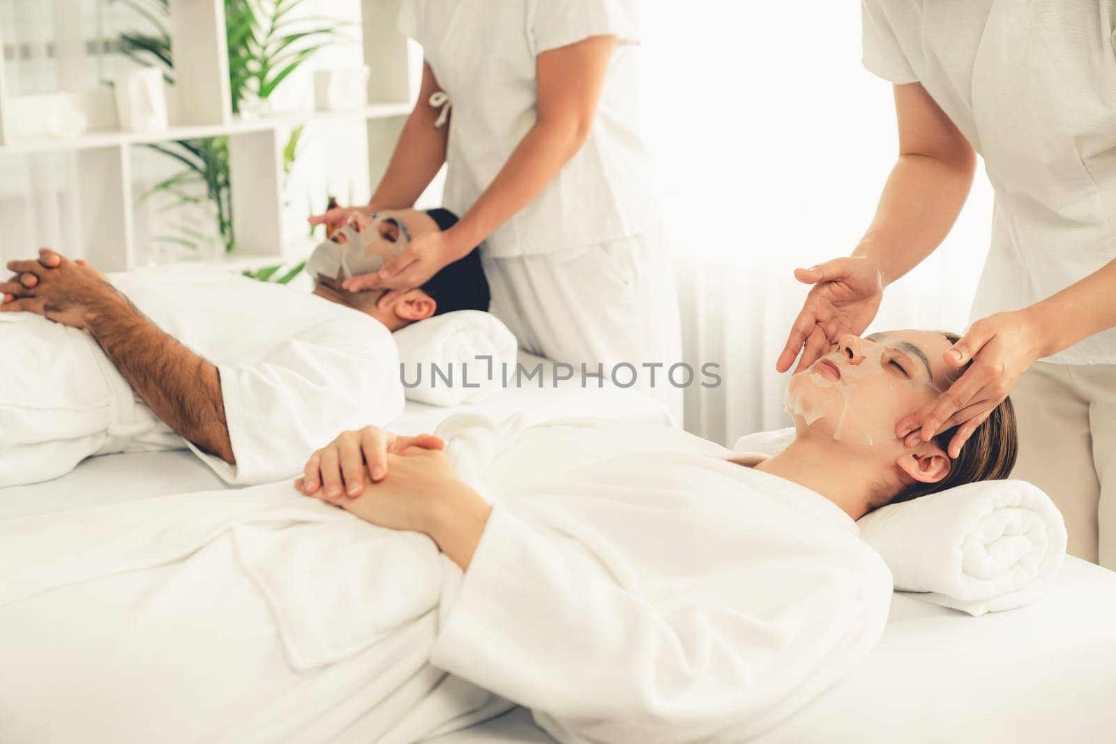 Serene modern daylight ambiance of spa salon, couple customer indulges in rejuvenating with facial skincare mask. Facial skin treatment and beauty cosmetology procedure for face. Quiescent
