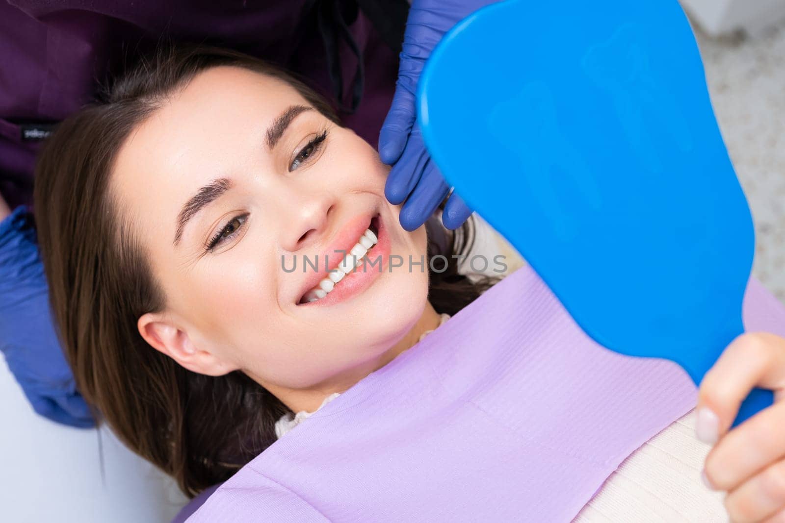 Smiling woman patient looks in the mirror after teeth whitening.