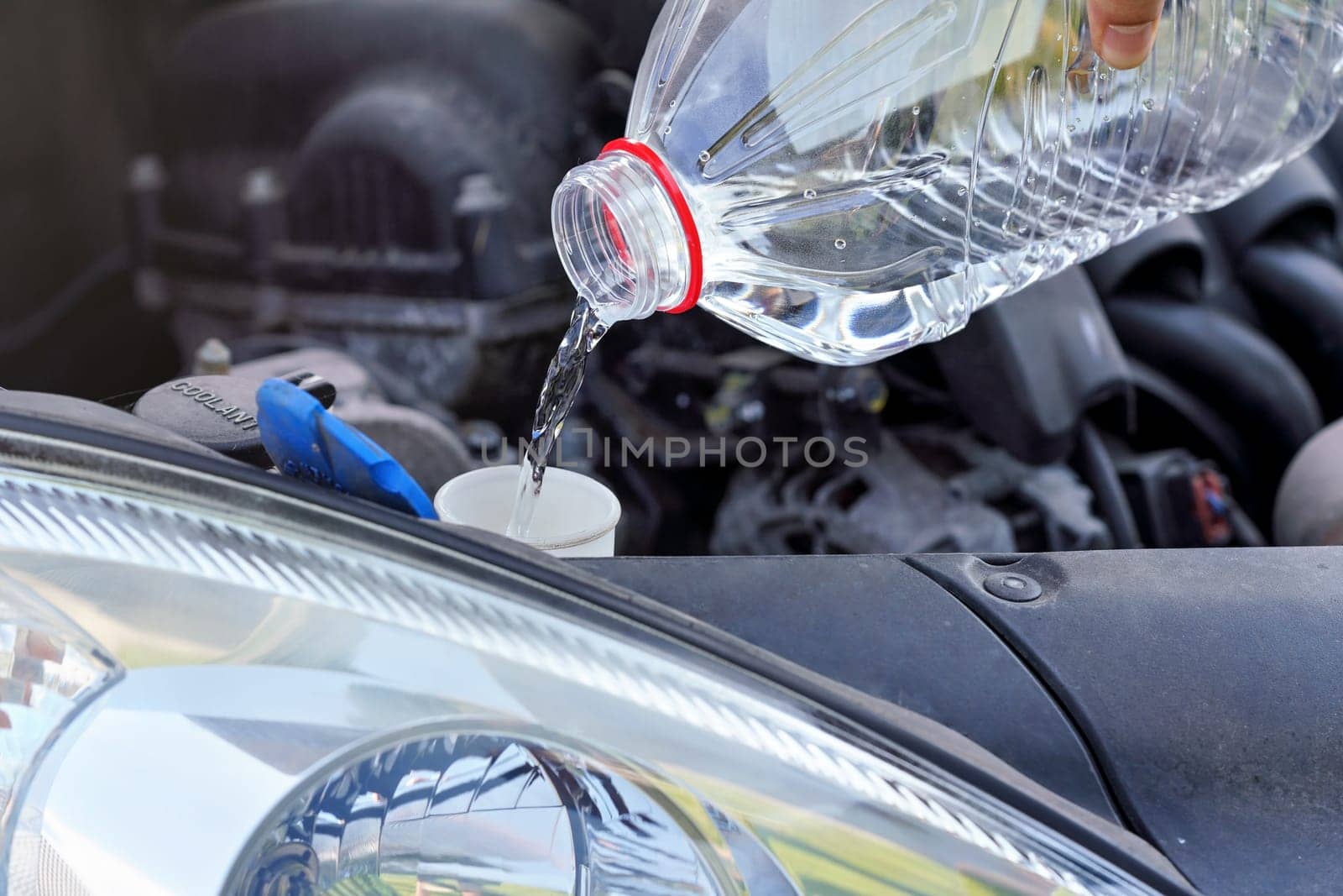 Pouring distilled water (ecological alternative to washing fluid) to washer tank in car, detail on liquid flowing from clear plastic bottle