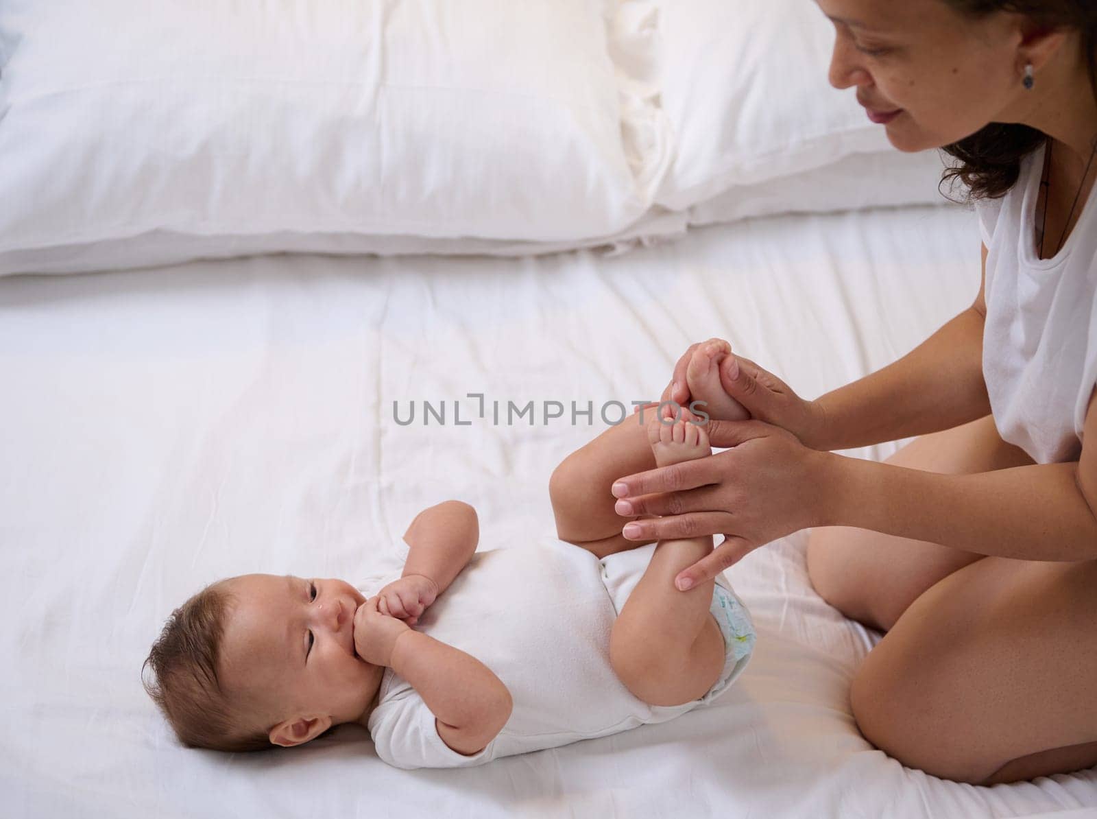 Beautiful newborn baby boy, looks at his loving caring mother stroking and kissing his little feet and tiny toes. by artgf