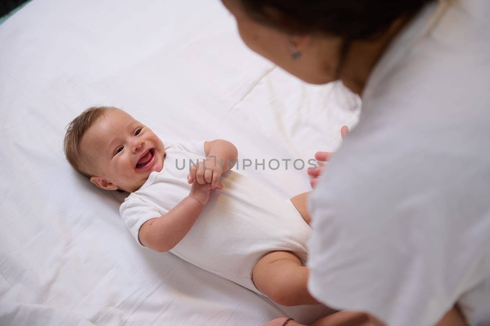View from above of a playful little baby boy 4 month old holding hands together, laughing, smiling, catching emotions of his loving caring mother. Smiling baby