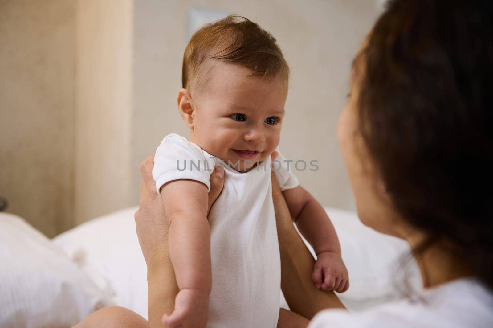 Happy excited newborn baby laughing at mother face, showing positive emotions. Mom talks with infant baby, laughs, throws up newborn baby in the air. Child and Mother day. Child and baby care concept.