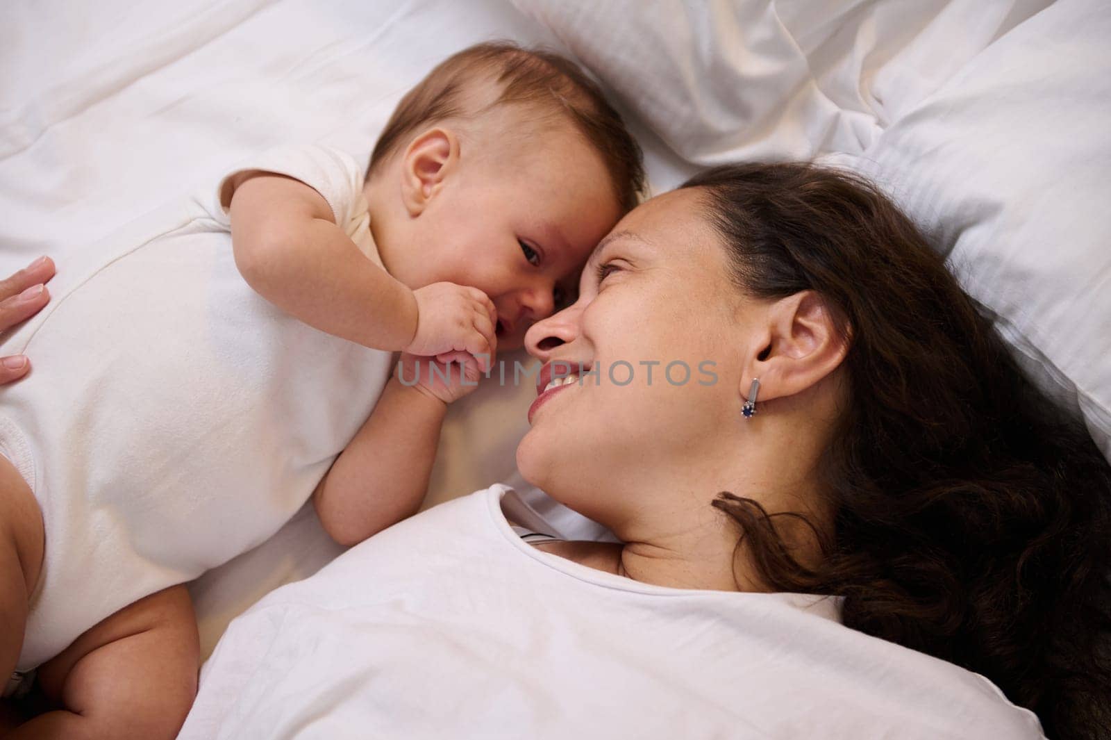 Close-up portrait of a happy smiling mother with her cute little baby lying on the bed, feeling emotional contact. Family relationships. Babyhood. Child and baby care. Maternity leave and motherhood