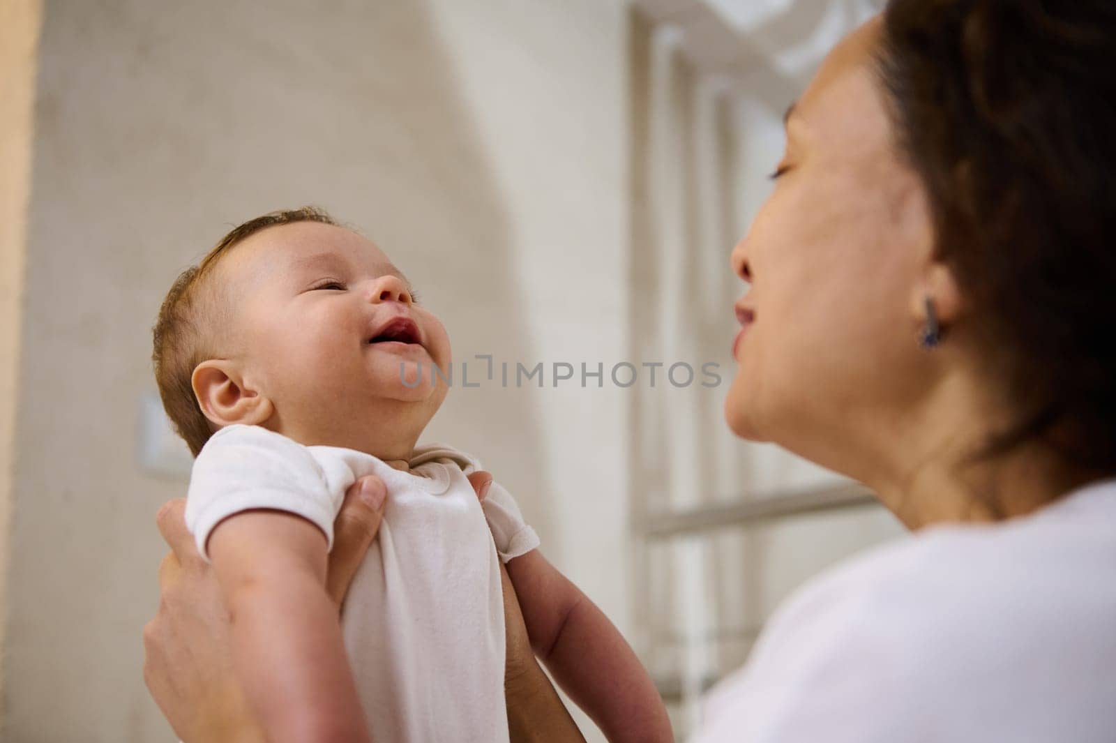 Close-up authentic portrait of a baby boy expressing positive emotions, smiling and laughing being in the arms of mom by artgf