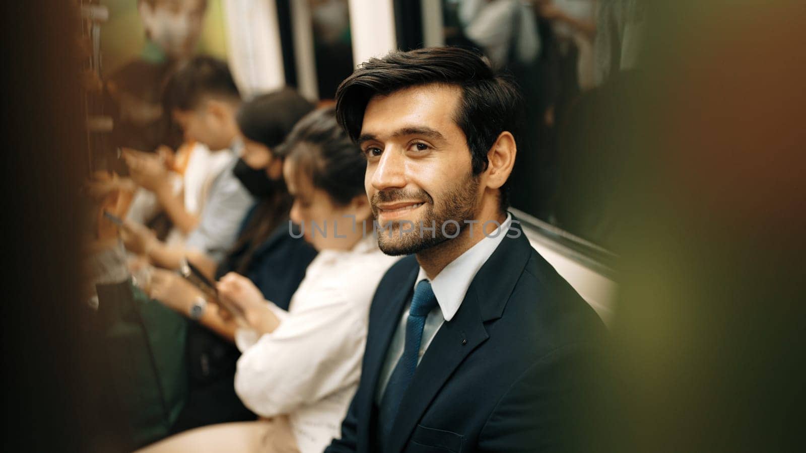 Smiling caucasian business man looking at mobile phone or playing social media while sitting in train. Attractive project manager going to work place by using public transport in rush hour. Exultant.