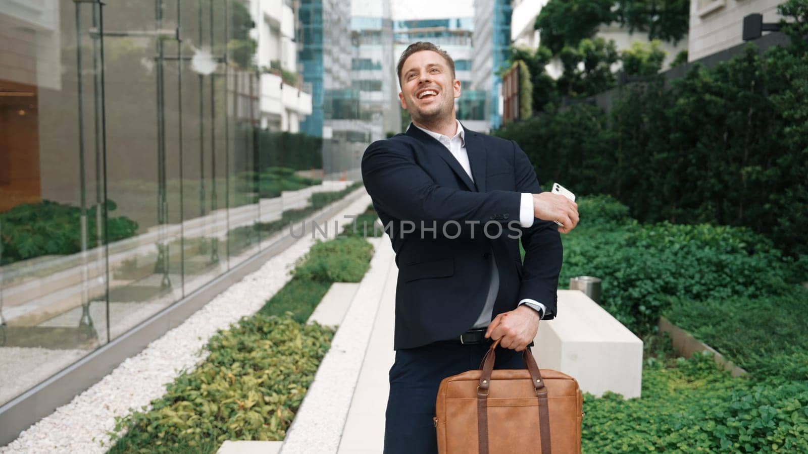 Professional caucasian businessman talking to manager by using phone while celebrated about increasing sales or getting promotion. Investor calling marketing team while walking at green city. Urbane.