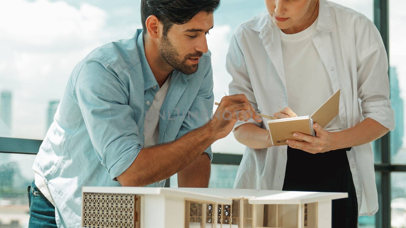 Skilled architect engineer team discussion about house model construction. Smart interior designer sharing, talking about building design while beautiful coworker taking a note. Design. Tracery