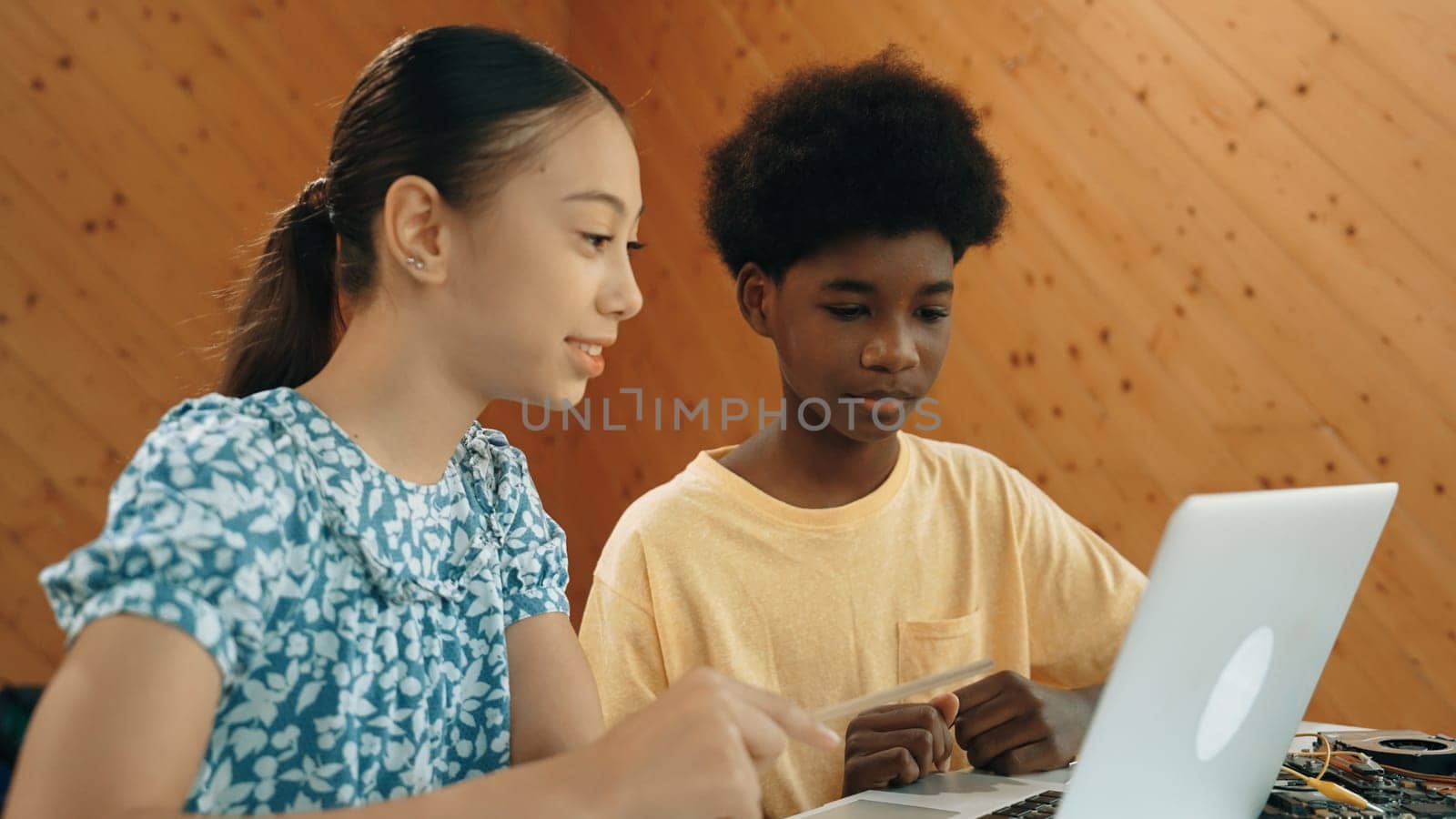 Site view of african boy and caucasian girl in casual cloth working together to coding prompt or programing system at table with laptop and electronic equipment at STEM technology class. Edification.