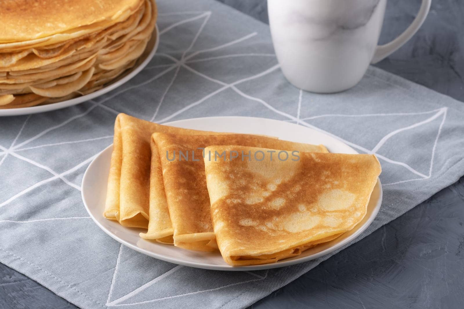 A stack of thin pancakes on a grey table.