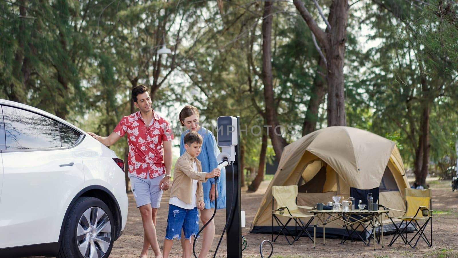 Outdoor adventure and family vacation camping in nature travel by eco friendly car for sustainable future. Lovely family recharge EV car with EV charging station in campsite. Perpetual