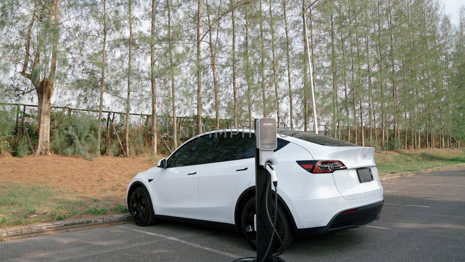 EV electric vehicle recharging battery from EV charging station in national park or outdoor forest scenic. Natural protection with eco friendly EV car travel in the autumnal season woods. Exalt