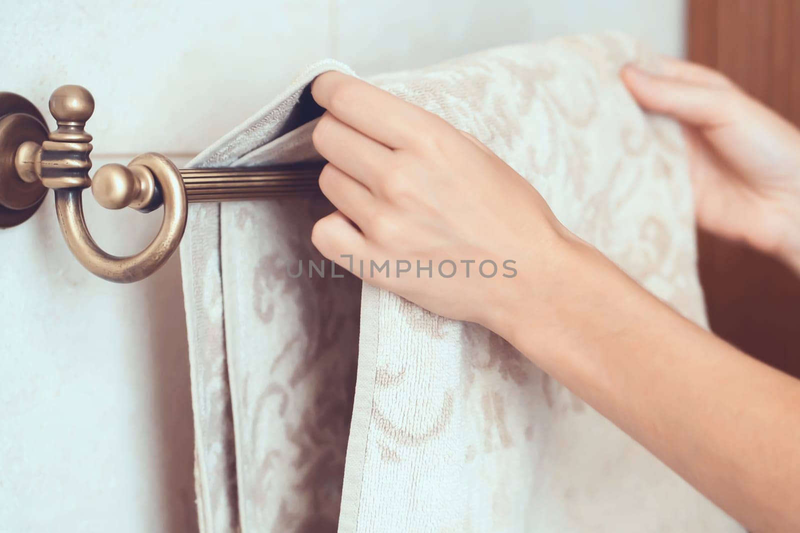 Female hands hang a fresh clean towel on a towel holder made in vintage style in the bathroom.