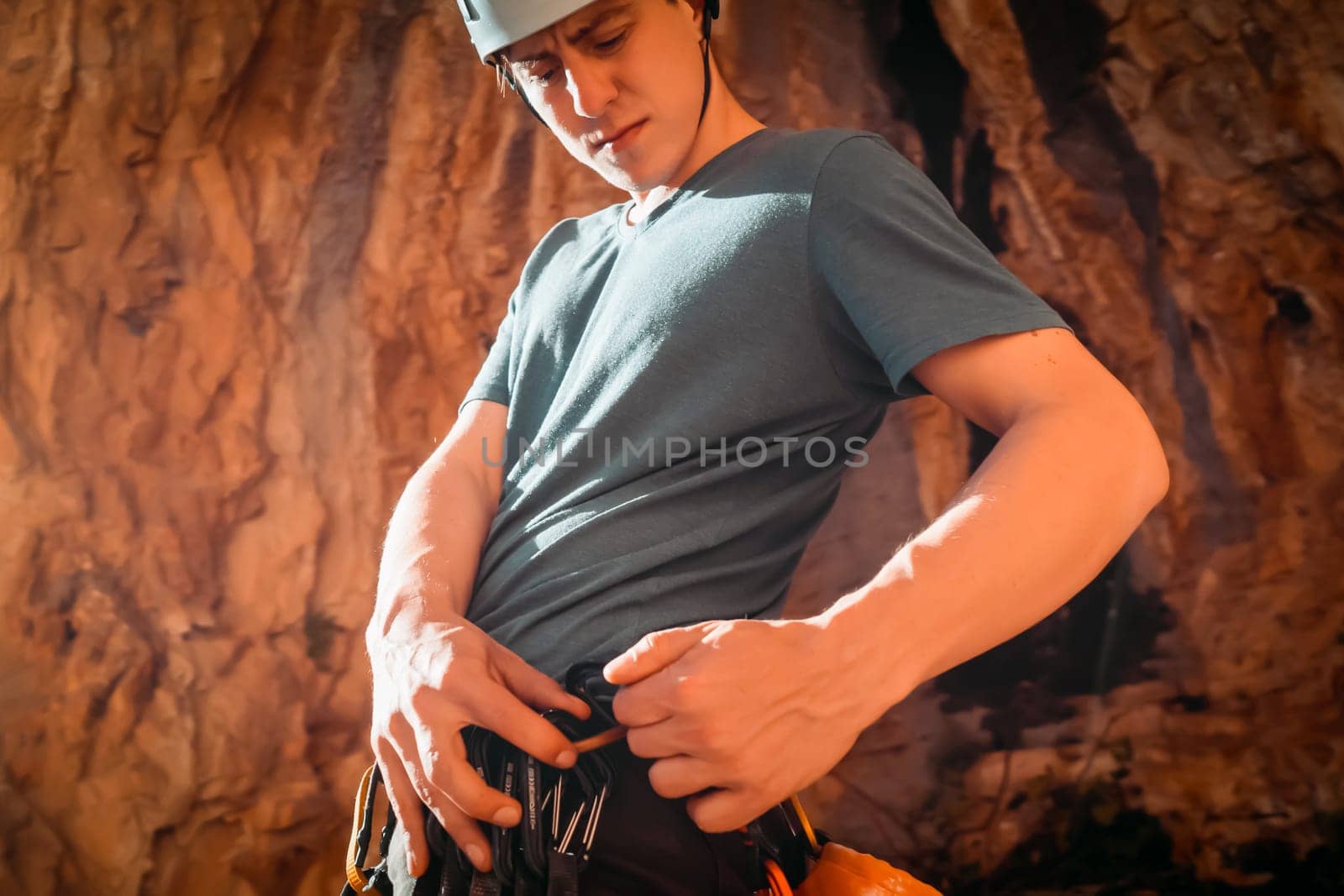 A man holds a carbine in his hand and fastens it to his climbing harness, the athlete is preparing for training on red rocks, is involved in active sports, rock climbing and mountaineering.