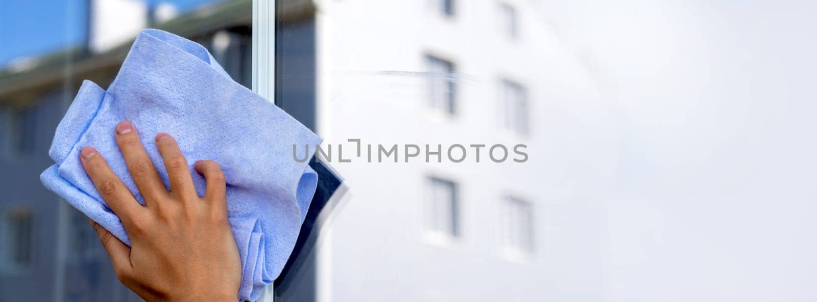 Woman cleans her house, female hand holds a rag and with detergent washes the window to perfect condition, a modern building is reflected in the window close up view with creative concept.