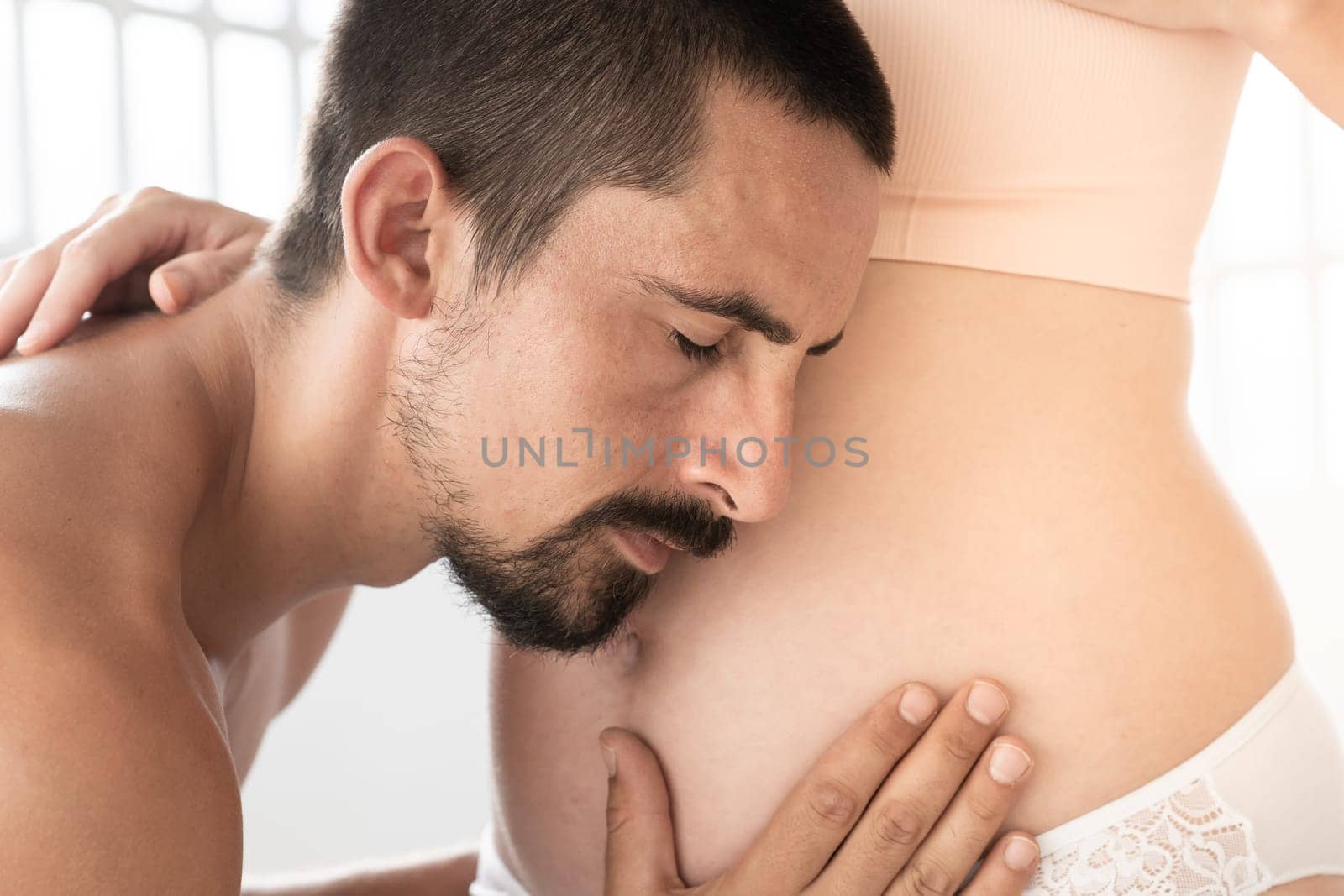 Man tenderly listening baby on round belly of a pregnant woman. His hand cradling it with love and affection. High quality photo