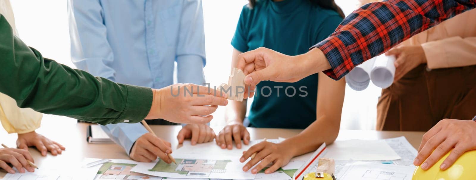 A cropped image of architect cooperate with engineer to build house during engineer team draft the blueprint on table with architectural equipment scatter around. Focus on hand. Delineation.
